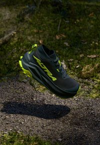 Czarne buty sportowe z neonowymi żółtymi akcentami, z teksturowaną cholewką, wyściełanym kołnierzem i solidną podeszwą, zawieszone nad leśnym dnem.