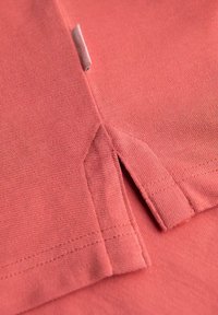 Koralli puuvillakangas, jossa on teksturoitu kudos, sivureikä ja ommeltu helma, esittelee siistin ja yksinkertaisen muotoilun.