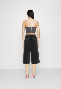 Grå denim bustier-top med dragkedja i ryggen, i kombination med lösa grå culottes och rosa blockklacksandaler, sedd från baksidan.