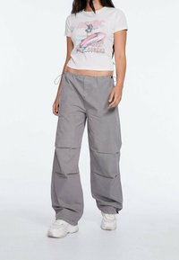 Pantalones cargo grises de corte relajado, con múltiples bolsillos y cinturilla con cordón. Combinados con una camiseta gráfica blanca ajustada.