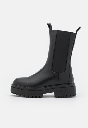 Bottines noires en cuir lisse, dotées de panneaux élastiques sur les côtés, de languettes de tirage, d'une semelle épaisse et d'un profil texturé pour une meilleure adhérence.
