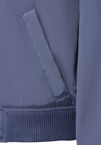 Marineblaue Bomberjacke mit geripptem Saum und glattem Stoff. Verfügt über eine Seitentasche mit rechteckiger Öffnung und verstärkten Nähten.