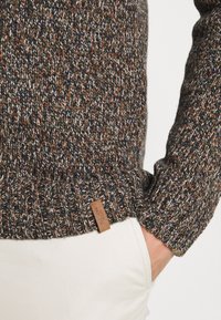 Gestrickter Pullover in dunklen Tönen mit Sprenkeln in Orange, Creme und Marineblau. Verfügt über gerippte Bündchen und ein Lederetikett der Marke am Saum.