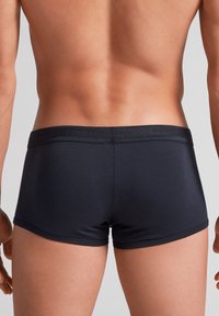 Boxers negros confeccionados en una tela suave, con una cinturilla blanda que presenta un detalle de logo texturizado. Diseño ajustado, de longitud hasta medio muslo.