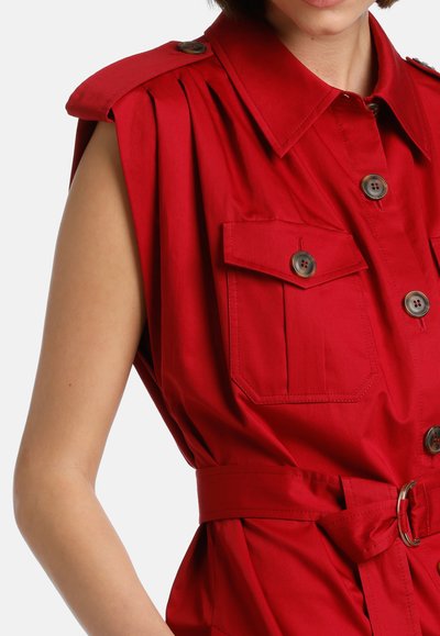 Red shirt with shoulder pleats, two front pockets, and a belted waist. Features button closures and a collared neckline. Smooth fabric texture.