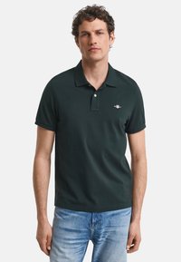 Mörkgrön polotröja i bomull, med klassisk krage, korta ärmar och en liten broderad logotyp på vänster bröst.
