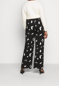 Pantalones de pierna ancha negros con un patrón abstracto de pinceladas blancas, hechos de una tela ligera, combinados con un suéter de punto crema.