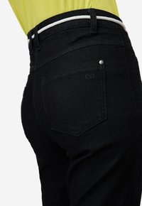 Jeans in denim neri con un design aderente, con tasche posteriori visibili e un rivetto argentato. La vita presenta una striscia di accento bianca.
