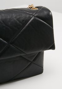 Borsa a tracolla in pelle nera trapuntata con forma strutturata, caratterizzata da motivi a diamante e dettagli in hardware dorato.