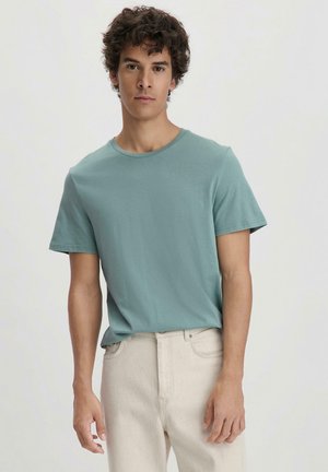 Helles Teal-T-Shirt mit kurzen Ärmeln aus weichem Stoff, mit Rundhalsausschnitt und lockerem Schnitt, kombiniert mit off-white Jeans.