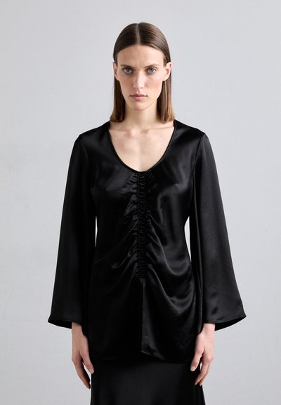 Top de satén negro con un profundo escote en V, centro fruncido y mangas largas y fluidas. La tela tiene una textura suave y brillante.