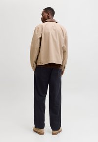 Μπεζ σακάκι με καφέ γιακά, σε συνδυασμό με σκούρο παντελόνι. Το σακάκι έχει χαλαρή εφαρμογή και ορατές λεπτομέρειες ραφής. Ελαφριά υφή, casual σχεδιασμός.