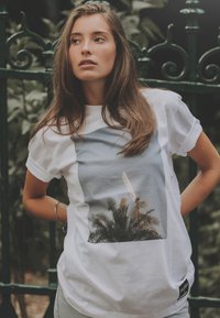 Witte t-shirt met een grafische print van palmen en een structuur, met een blauwe achtergrond. Korte mouwen en een zijlabel met 'GLORY'.