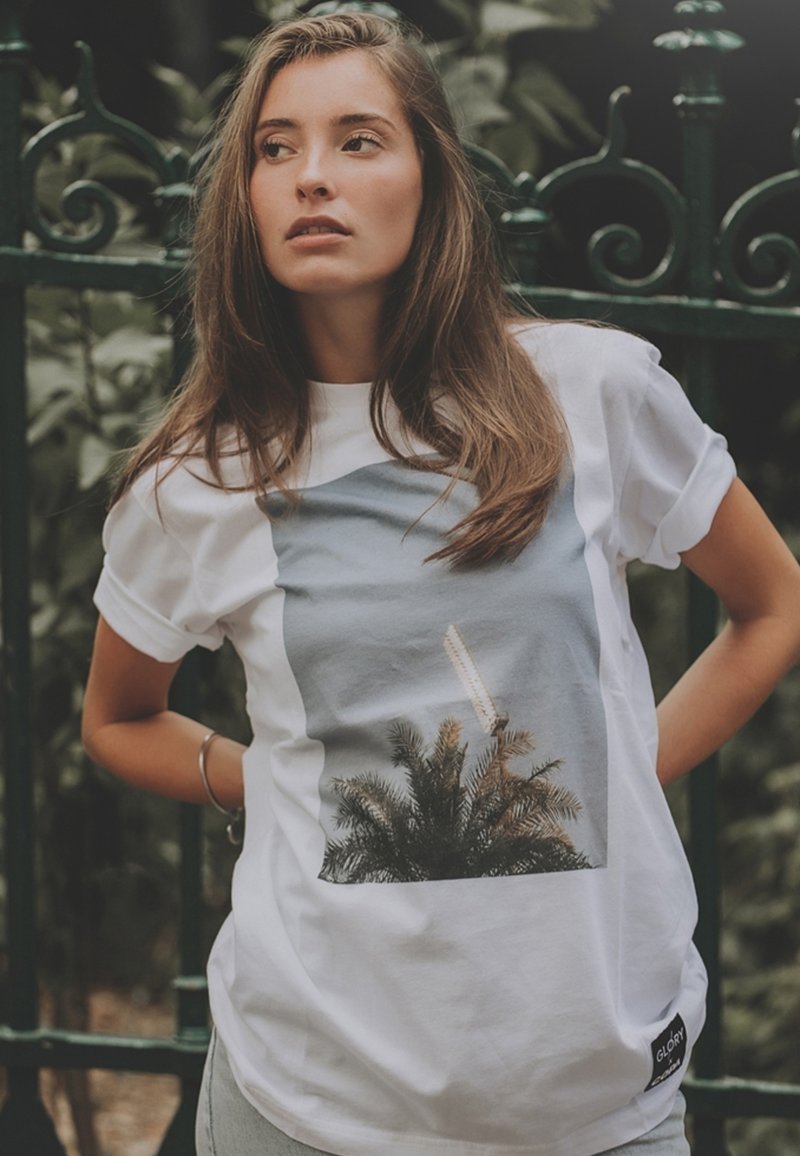 Witte t-shirt met een grafische print van palmen en een structuur, met een blauwe achtergrond. Korte mouwen en een zijlabel met 'GLORY'.