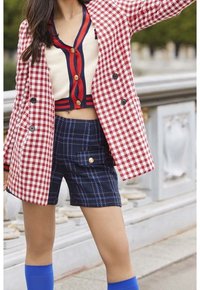Red and white houndstooth blazer, buttoned at center; cream top with red and navy accents; navy plaid shorts with gold button detail; blue knee-high boots.