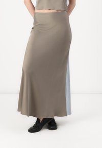 Jupe longue et ajustée en vert olive, fabriquée en matière lisse et extensible avec un ourlet évasé. Associée à des chaussures noires à enfiler.