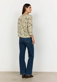 Bluse med blomsterprint i creme og blå, trekvartærmer, kombineret med mørkeblå lige jeans og brune kilehæle.