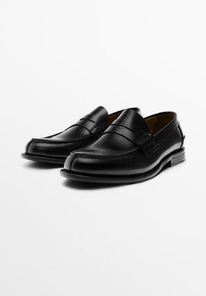 Svarta läderloafers med slät finish, rundad tå och dekorativ remdetalj. Har en låg staplad klack och subtila sömnadsdetaljer.