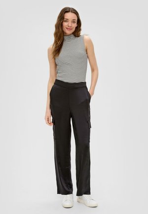 Top a righe senza maniche con scollo alto, abbinato a pantaloni cargo neri in satin con tasche laterali e vestibilità rilassata. Sneakers bianche.