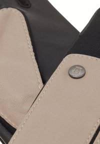 Schwarze und beige Lederhandschuhe mit kontrastierenden Einsatzflächen, sichtbaren Nähten und einem runden, silbernen Druckknopf mit eingraviertem Design.