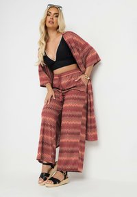 Tvådelad outfit med en kimonojacka i zigzag-mönster och vida byxor i röda och orange nyanser, kombinerad med en svart topp och espadrillosandaler.