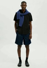 Juodas trumpas rankovėmis marškinėliai, tamsiai mėlynos trumpinės, tamso mėlynas megztinis ant pečių, juodos kojinės ir juodi batai. Švarus, paprastas ir prigludęs dizainas.