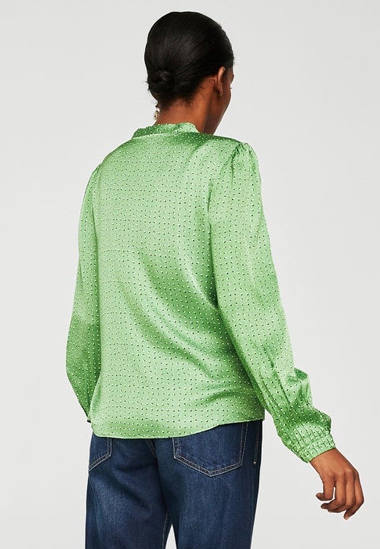 Blusa verde in satin con maniche lunghe, spalle arricciate, texture a pois e polsini arricciati. La vista posteriore mostra un collo rotondo e una vestibilità ampia.