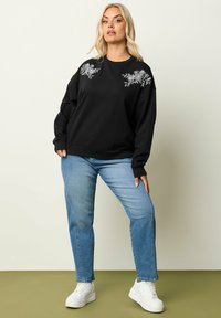 Felpa nera con ricami floreali sulle spalle, caratterizzata da una vestibilità morbida. Abbinata a jeans azzurri chiari e sneakers bianche.