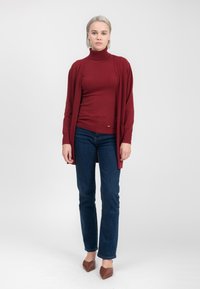 Burgundy polokrave under en åben cardigan, parret med mørkeblå jeans og brune spidse flade sko. Glat strikket stof med ribbede detaljer.