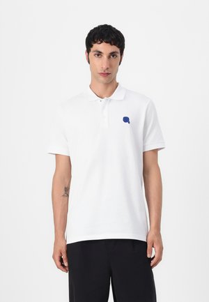 Hvit polo skjorte med krage, med en liten blå logo på venstre bryst. Korte ermer, myk stoffkvalitet og en klassisk passform.