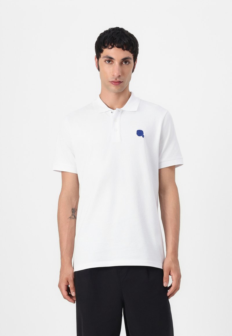 Biele polo tričko s golierom, s malým modrým logom na ľavom hrudníku. Krátke rukávy, mäkká tkanina a klasický strih.