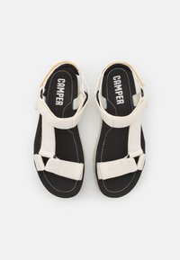 Svarta sandal med vit justerbar tygremmar och "CAMPER"-logotyp på innersulan, visade från ovan mot en vit bakgrund.