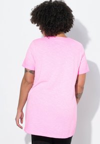 Roze, kortemouwen T-shirt van zacht materiaal, met een relaxte pasvorm en een verlengde achterzoom. Eenvoudig ontwerp zonder zichtbare patronen.