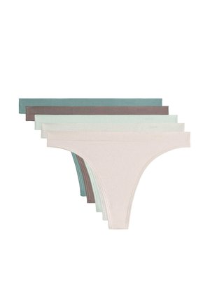 Žena nosi svetlozelené bezšvové bikiny, ktoré ukazujú pás, boky a hornú časť stehien na neutrálnej pozadí.