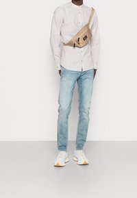 Helles Leinenhemd mit Rundkragen, beiger Gürteltasche, hellblauen Jeans und hellen Sneakers mit Akzenten in Beige und Grau.