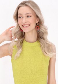 Top senza maniche di colore verde lime, realizzato in tricot con colletto alto, caratterizzato da un tessuto testurizzato. Persona con orecchini a cerchio di perline.