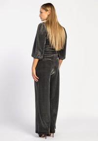 Fluwelen jumpsuit in donkergrijs met een getailleerde top, pofmouwen en wijde pijpen. Soepele textuur, minimale glans, met achterzakken.