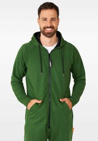 Sudadera con cremallera verde y capucha forrada en negro. Cuenta con dos bolsillos frontales y detalles de cremallera en contraste. Fabricada con un tejido suave y texturizado.