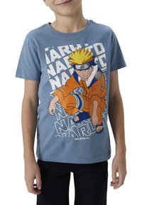 T-shirt en coton bleu avec un personnage vêtu d'orange, ayant des cheveux jaunes en piques, un bandeau et un design de texte dynamique en blanc.