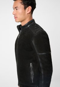 Schwarze Lederjacke mit hohem Kragen, Reißverschluss, seitlicher Tasche mit Reißverschluss und strukturierten Akzenten an Schultern und Ärmeln.