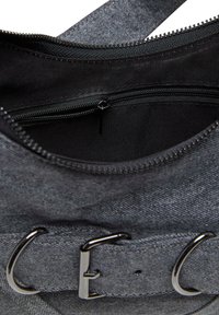 Grijze denim tasinterieur met een ritssluiting pocket, stevige zwarte voering en een metalen gesp accent op de schouderband.
