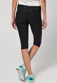 Černé capri legíny s texturovaným povrchem a růžovým akcentem na boku. Vyrobené z elastické látky pro pohyb a pohodlí.