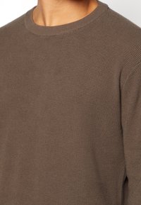 Pull en tricot marron texturé avec un col ras du cou. Le tissu semble doux avec un motif subtil en relief et une silhouette ajustée.