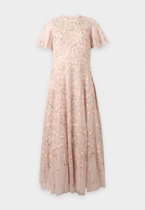 Femme portant une longue robe rose transparente avec broderies florales et manches volantées, associée à des mules à talons pointues de couleur claire.