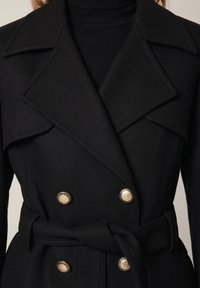Czarny, podwójnie zapinany płaszcz wełniany z szerokim kołnierzem, złotymi guzikami i paskiem w talii. Teksturowana tkanina z dopasowanym krojem i eleganckim designem.