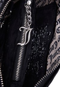 Ασημένια αλυσίδα με φερμουάρ και προσδεμένη καλλιγραφική γράμμα "J" σε φερμουάρ μαύρης υφής σε τσάντα επενδεδυμένη με μαύρο και άσπρο εκτυπωμένο κείμενο.