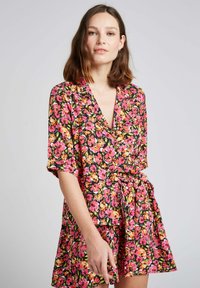 Robe à imprimé floral avec un fond noir, ornée de fleurs roses et oranges. Manches courtes, col en V et détail de taille nouée.