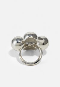 Anillo de metal plateado con tres acentos redondeados y lisos. La banda es brillante y presenta un logo grabado en la superficie interior.
