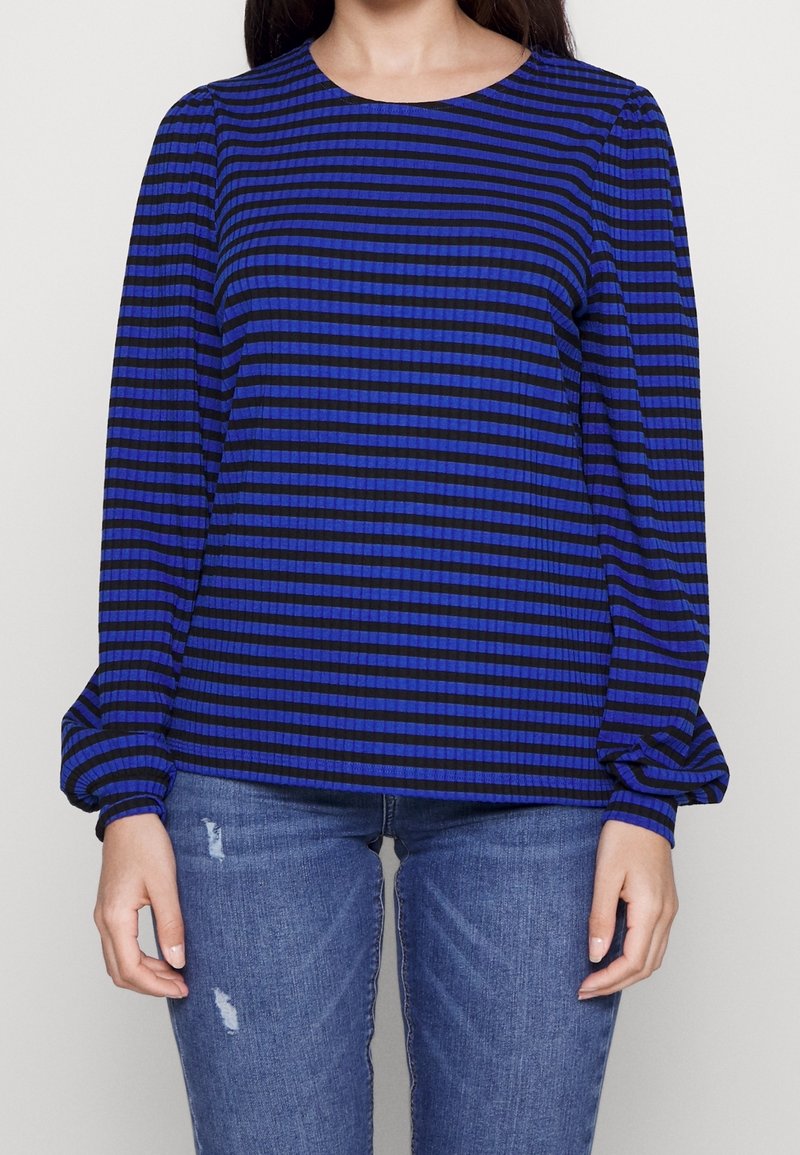Blue and black striped long-sleeve top with a rounded neckline and gathered sleeves, made of a textured fabric. Paired with distressed blue jeans.