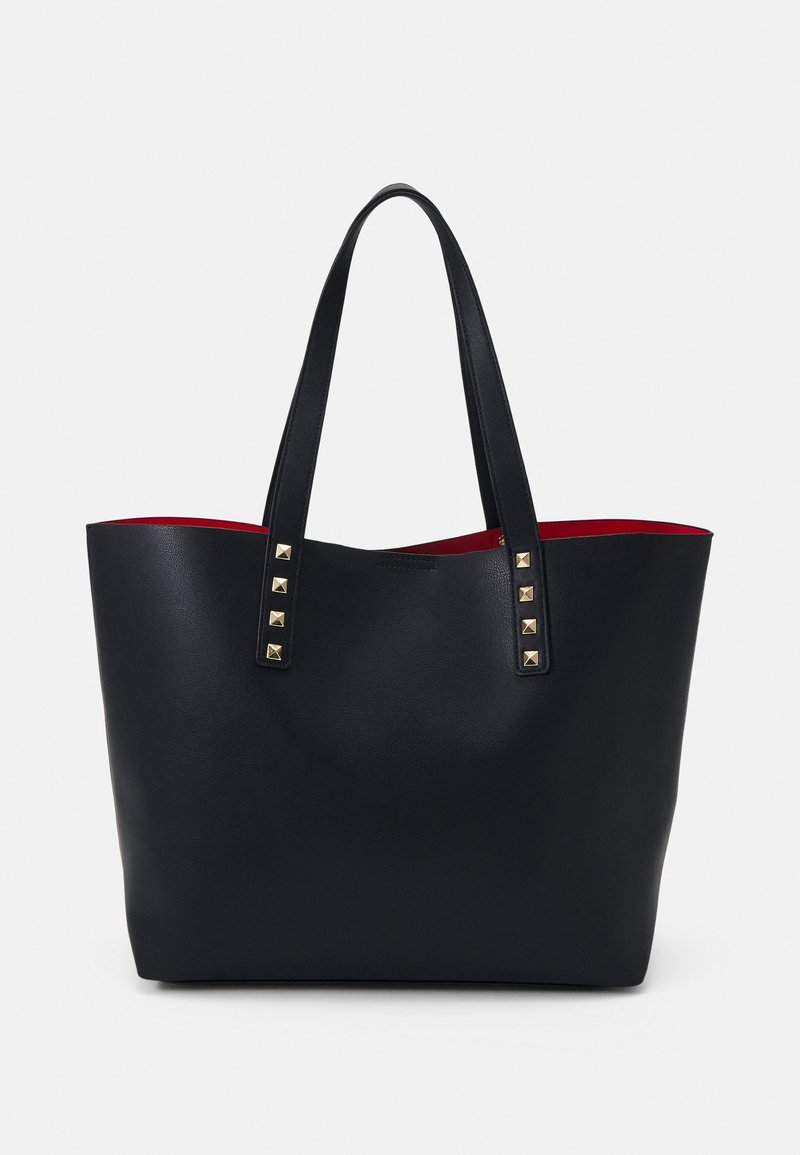 Sac cabas en cuir noir avec double poignée, clous carrés dorés sur les anses et doublure intérieure rouge, présenté sur un fond uni.